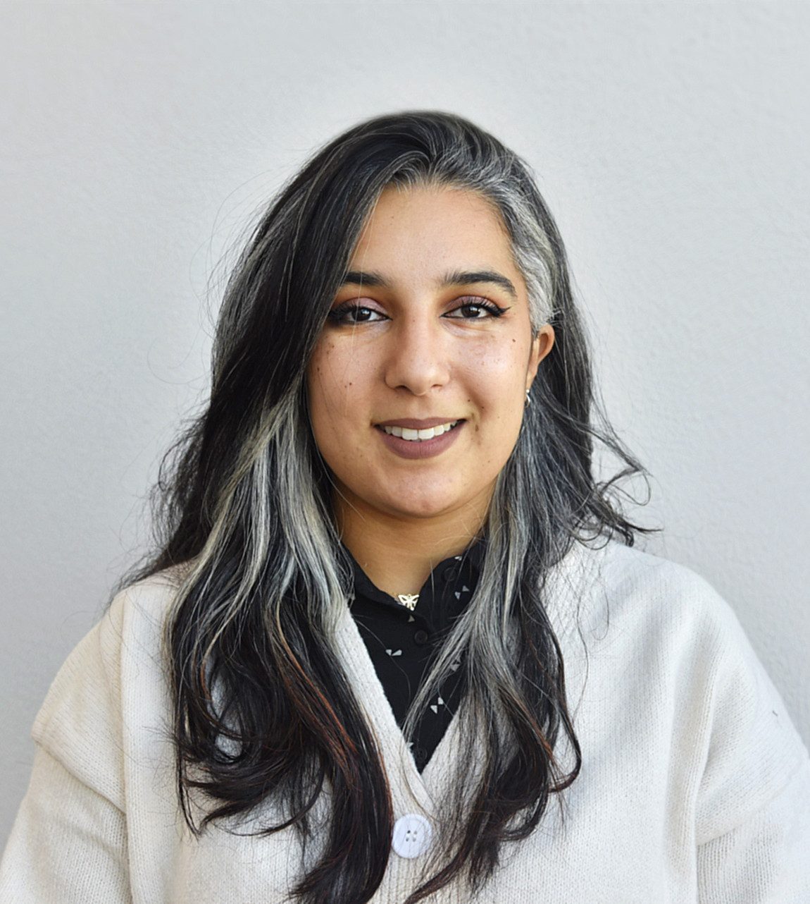 The picture shows a young woman with long, two-toned hair: she has dark hair with gray or white strands framing her face.